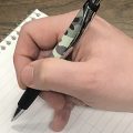 A hand holding a camo patterned pen on a pad of paper, poised.