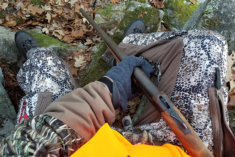 hunter looking down at his shotgun while sitting on a watch