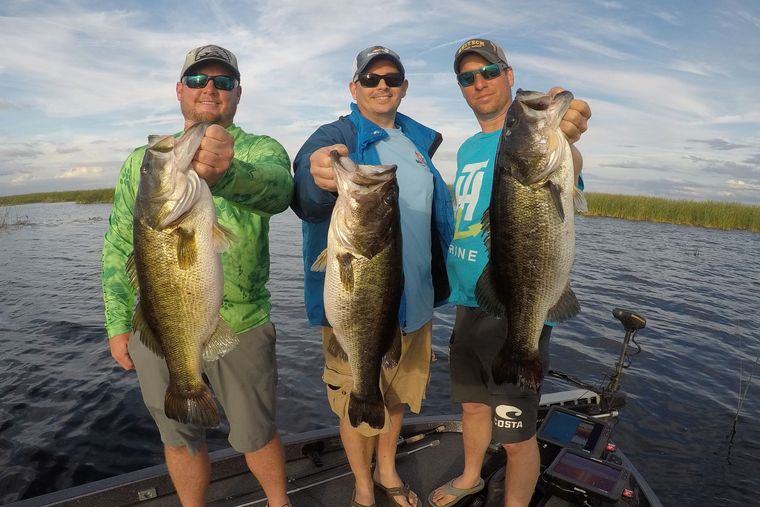 three anglers in a boat holding largemouth bass