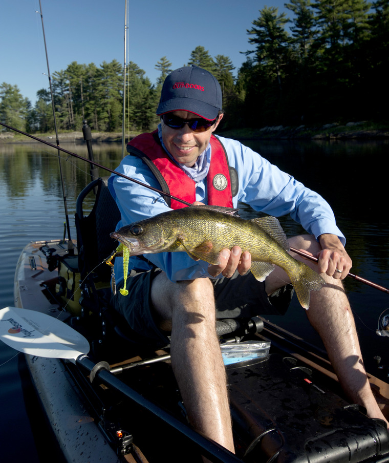 Tim Allard in a fishing kayak, holding a walleye. 