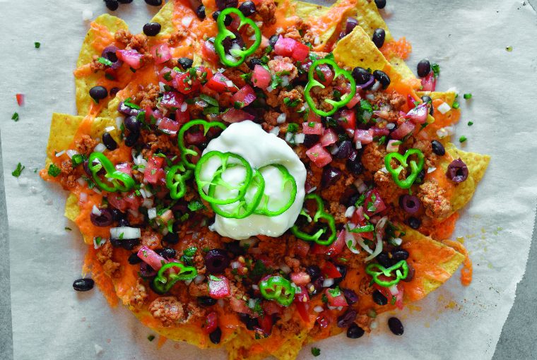 Baking sheet full of wild turkey nachos with beans, peppers, tomatoes, onion, and sour cream.